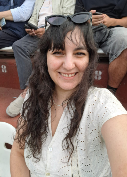 Woman with dark har and sunglasses sitting in a stadium seat smiling at the camera