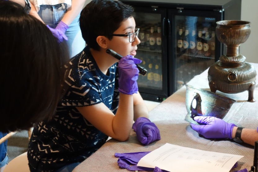 A student holds a flashlight up to an ancient pot