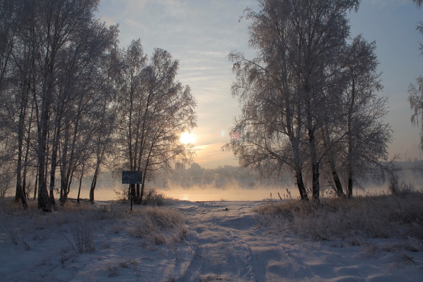 A sunset over a misty lake with snow and trees around