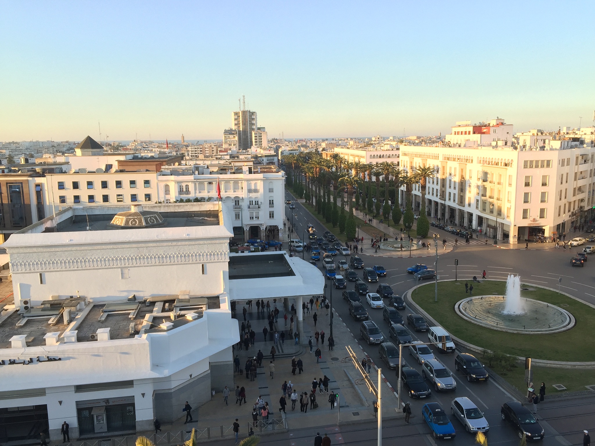 A city seen from above, with a busy street, fountain, and buildings