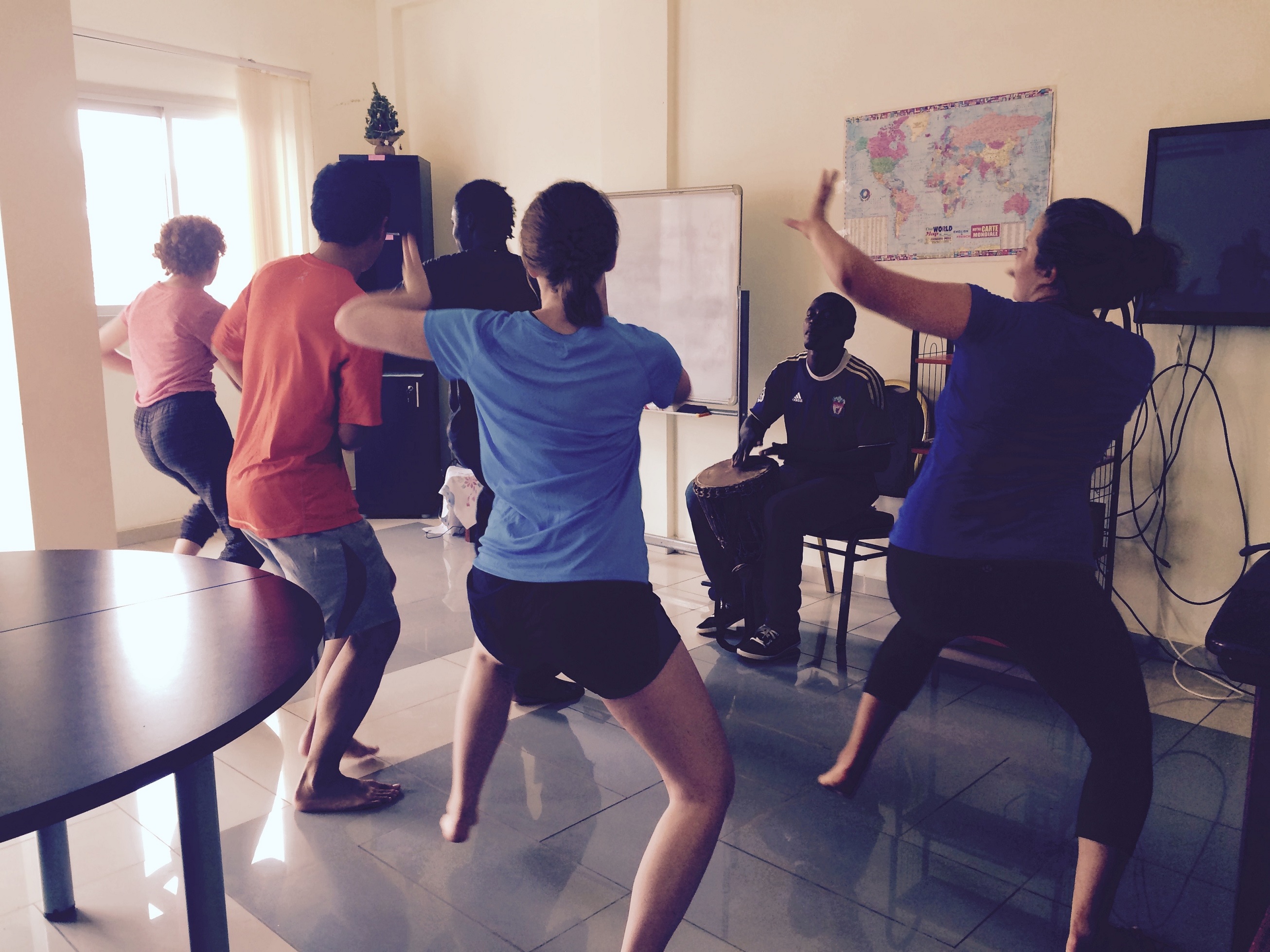Students learn to dance while a man plays a drum in front of them
