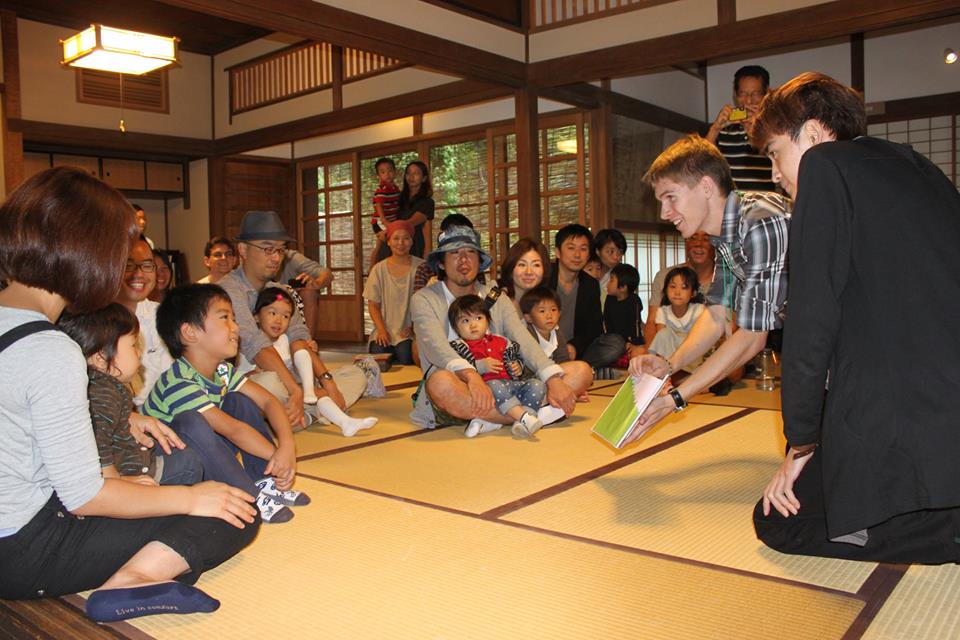 Students show pictures in a book to a group of small children and adults