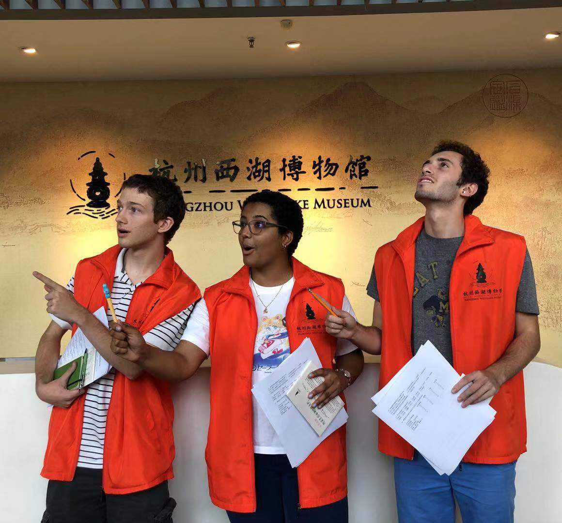 Students in red vests hold papers and indicate something out of sight