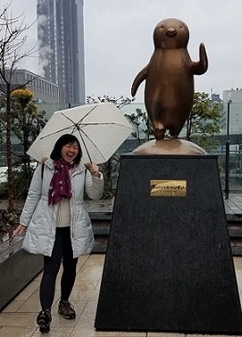 A student stands by a cute statue in the rain