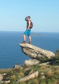 A student standing on a boulder and looking out across the ocean