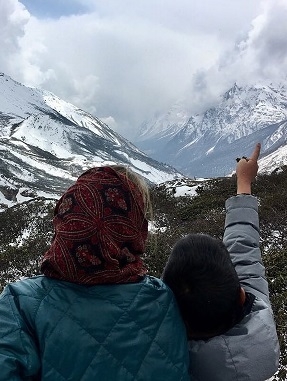 A young boy points at a snowy mountain while a student looks on