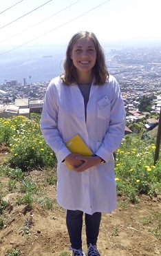 A student stands on a hill overlooking the bay, wearing a lab coat