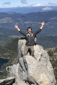 A student stands on a boulder with a mountain view behind him