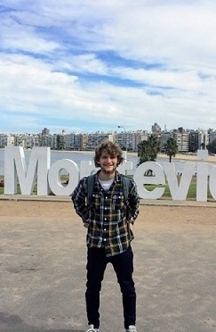 A student stands on the beach in front of a sign that says "Montevideo"