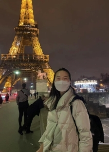 A student with a mask on in front of the Eiffel Tower at night