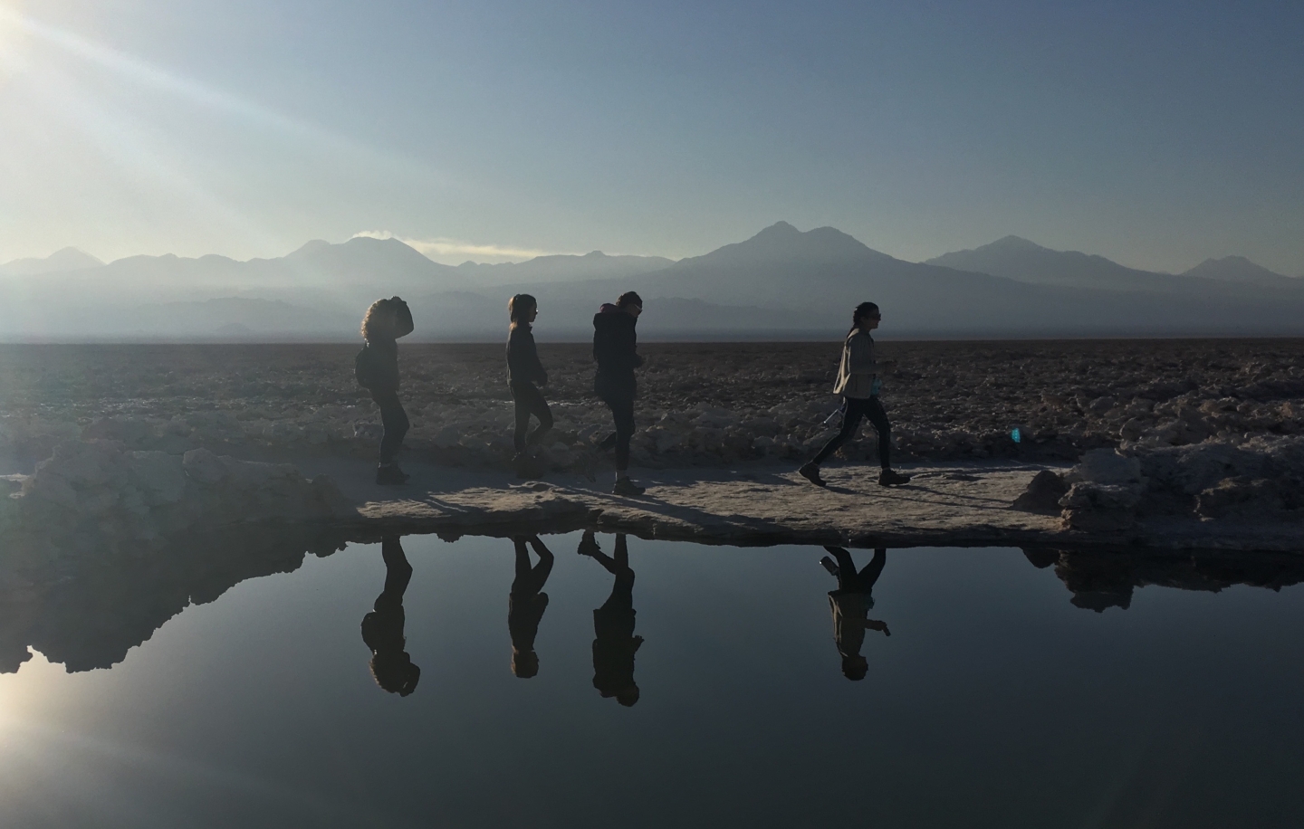 Four students walk in the desert. Their reflections are seen in a pool.
