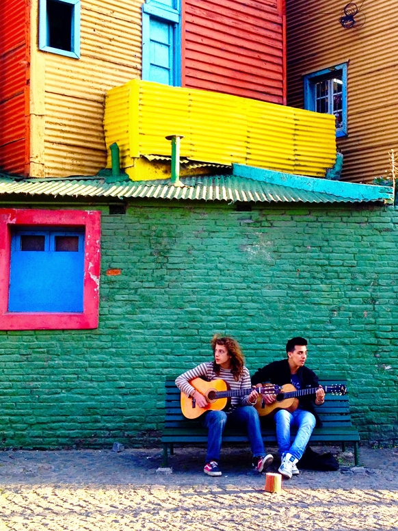 Two students playing music while leaning against a wall in Argentina