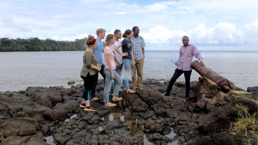 Students sitting and standing on rocks near shore