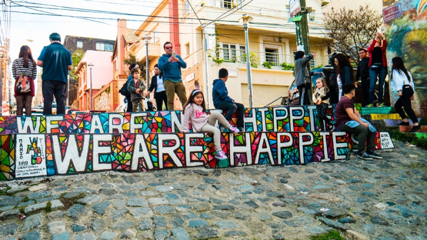Local children climbing on big art sign reading We Are Happy