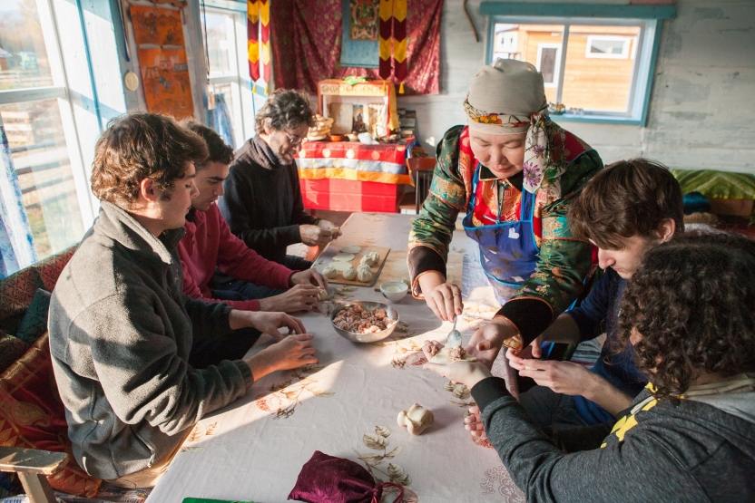 A woman fills a dumpling in the hand of a student, with others around a table