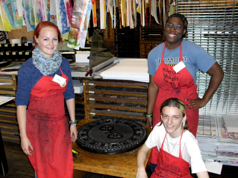 Students with smocks stand in front of hanging prints