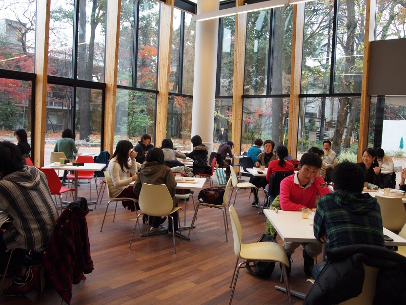 Students sit in a dining hall with large windows showing the campus outside