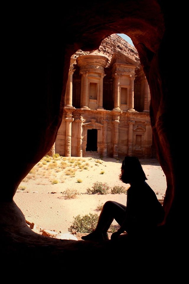 A student sits in a shadow looking at the archaeological city of Petra