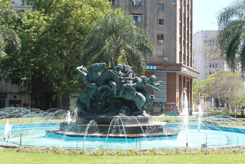 A fountain in a park with statues of people on horses