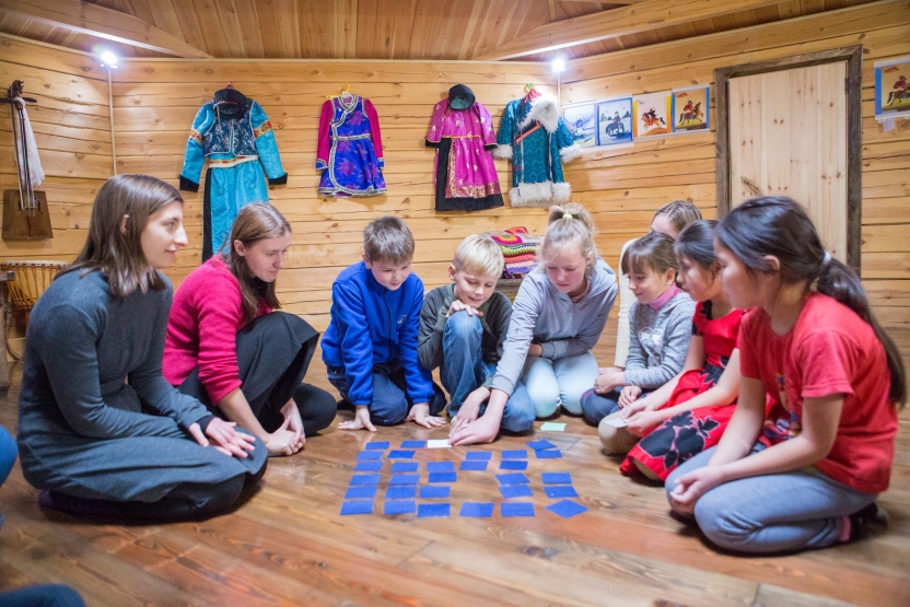 A student plays games with children, all sitting on the ground