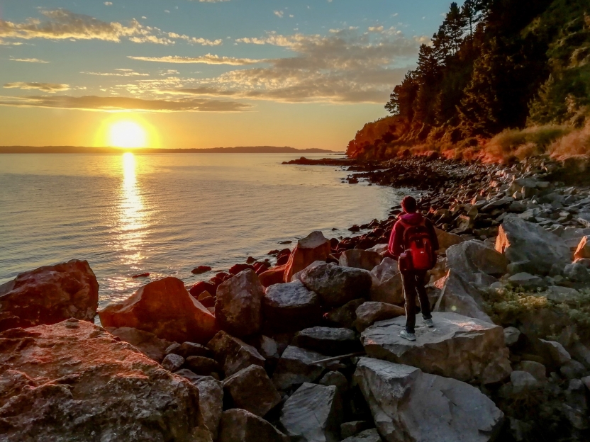 A sunset over a beach with a student walking on rocks