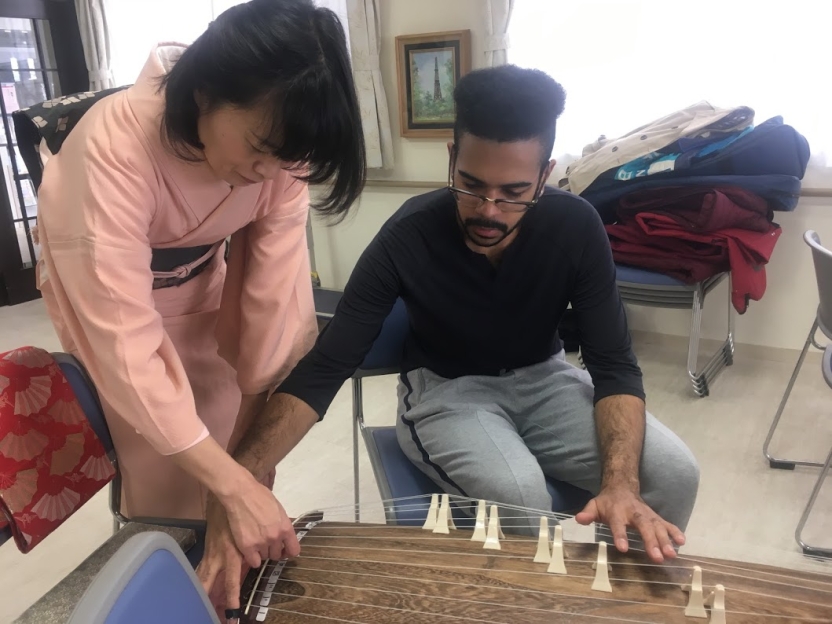 A student learns to play a stringed instrument from a teacher in a kimono
