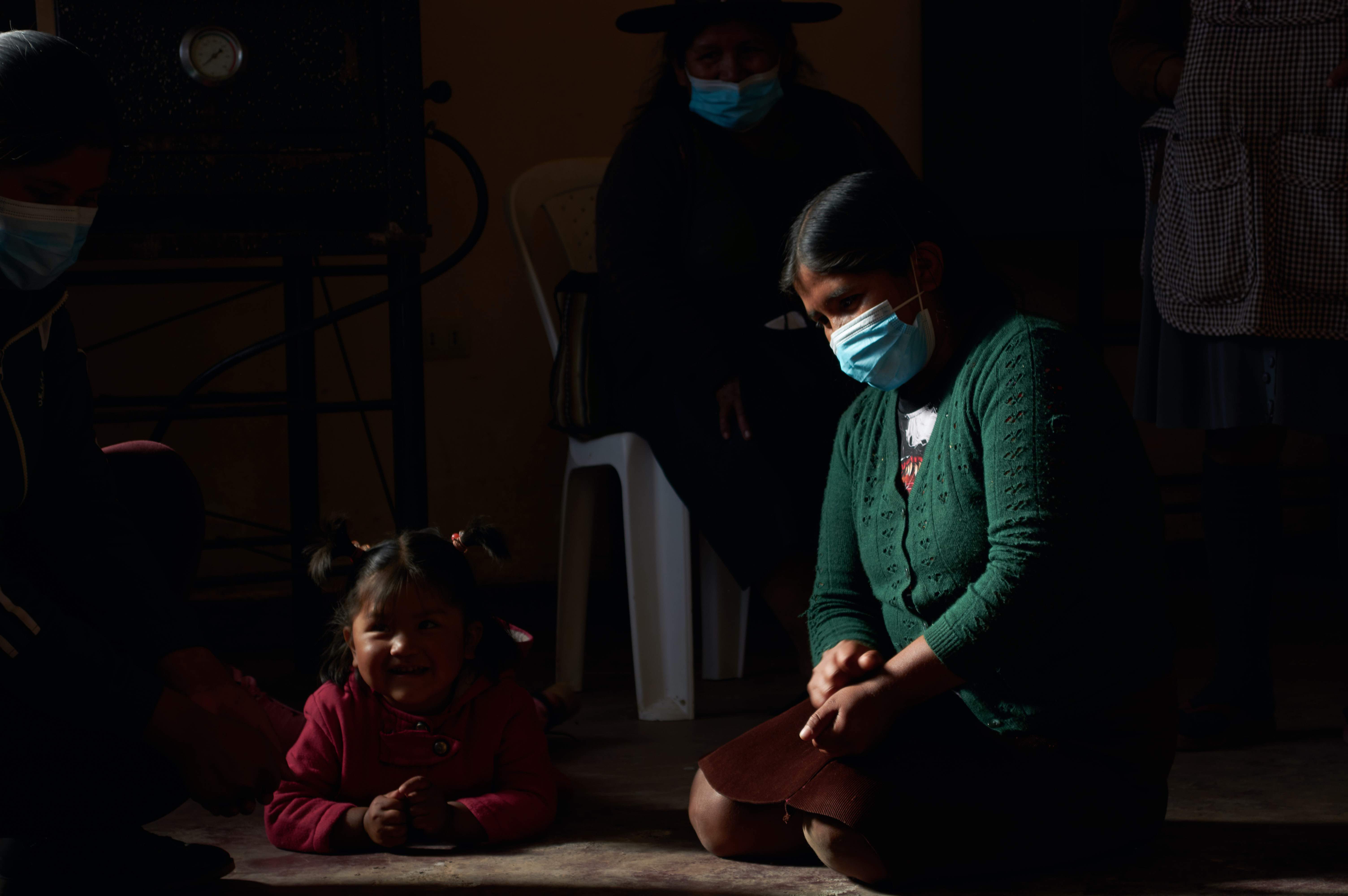 A woman in a mask sits next to a smiling little girl