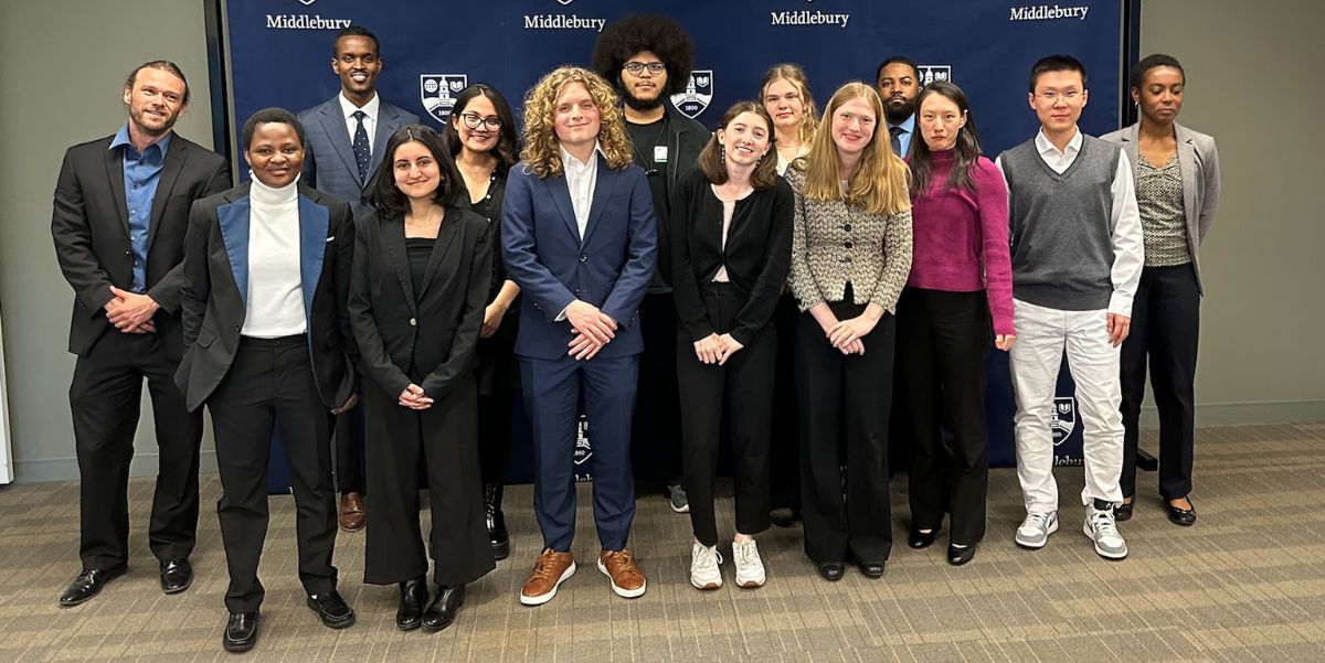 A group of students posing in fron of a Middlebury College backdrop. They are dressed in bbusiness attire.