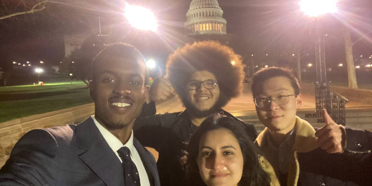 4 students pose in front of the white house at night.