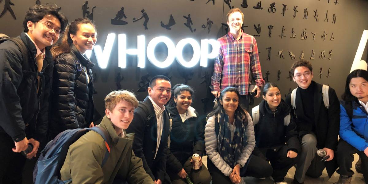 A group of students and staff pose in front of the Whoop sign.