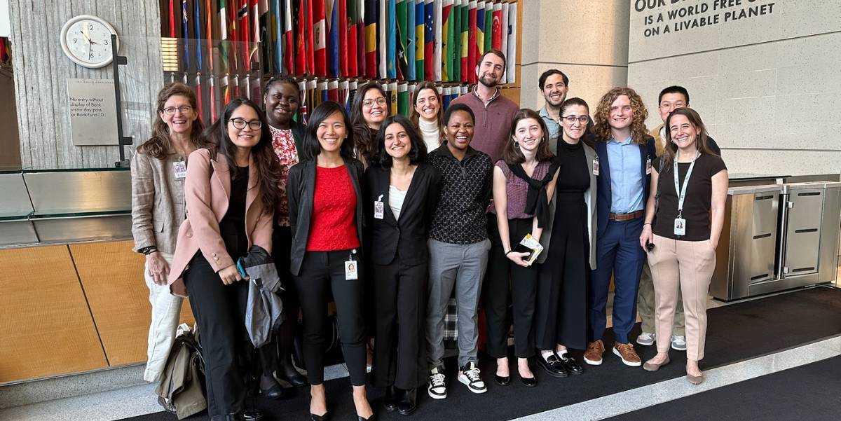 A group of students pose in front of the international flags in the lobby.