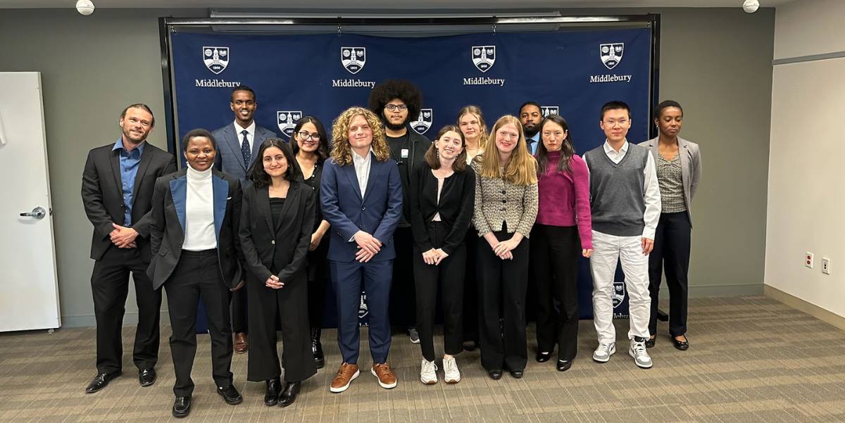 A group of students post in front of a Middlebury background at the Middlebury in DC office.