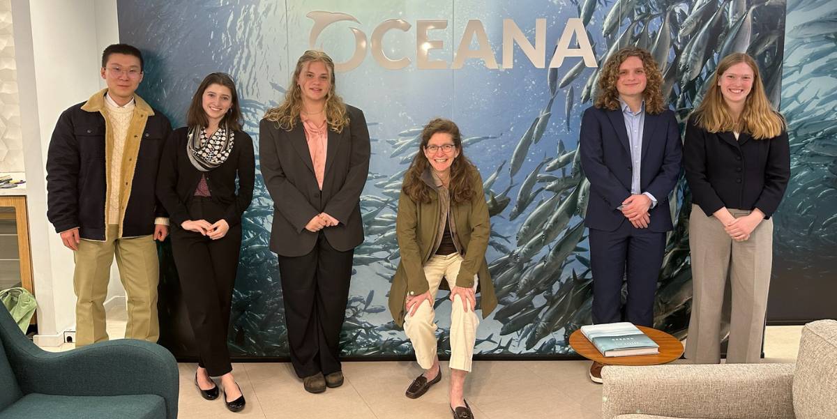5 students and Tracy Himmel Isham pose in front of the Oceana logo.