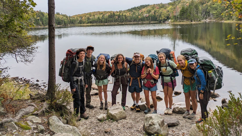 Students on a backpacking trip pause by a lake.