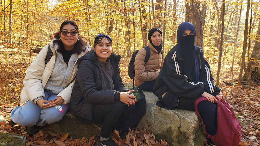 A groups of students pause to rest while walking in the woods in Fall.