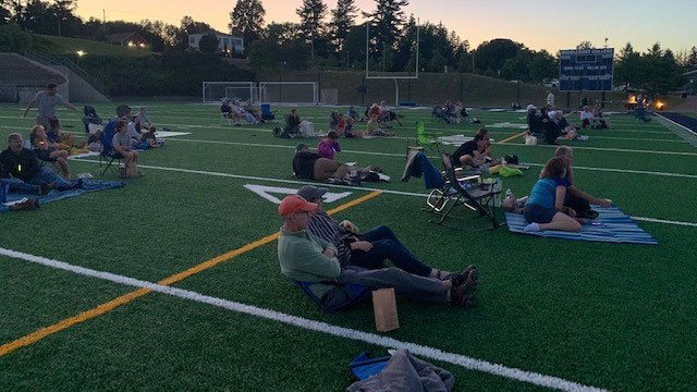 employees outside watching movie on football field at dusk