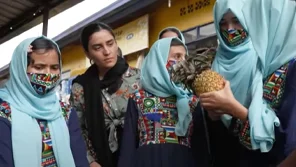 A group of Afgan girls are standing together while one is holding a pinapple.