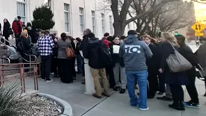 A group of people stand in a long line outside of a building.