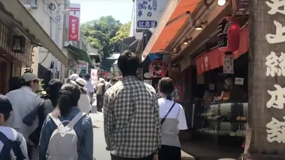 People walking down a busy street in Tokyo in the daytime surrounded by little shops.