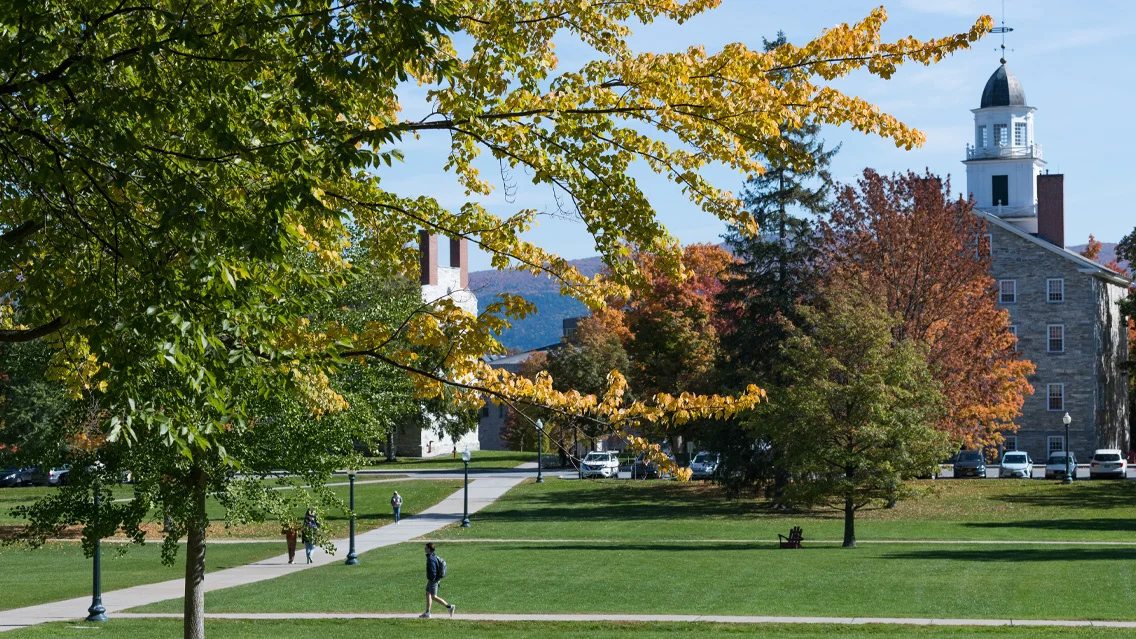 A view from the college quad looking at the back of Old Chapel. Students walk along the path beneth trees that are turning colors in early Autumn.