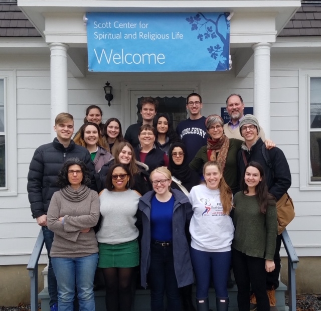 group of 18 students and Scott Center staff on front porch of Hathaway House, beneath a "Welcome" banner