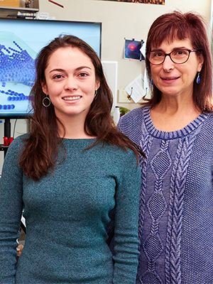 Professor Grace Spatafora standing by Michelle Lehman, with a glimpse of a computer rendering of bacteria on a screen behind them.