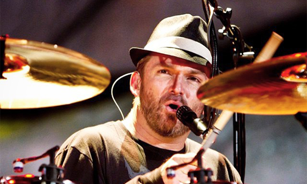 Brad Corrigan in fedora and tshirt, singing & playing drums