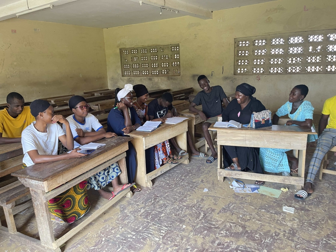 A group of young men, young women, and teachers chat and smile in a classroom.