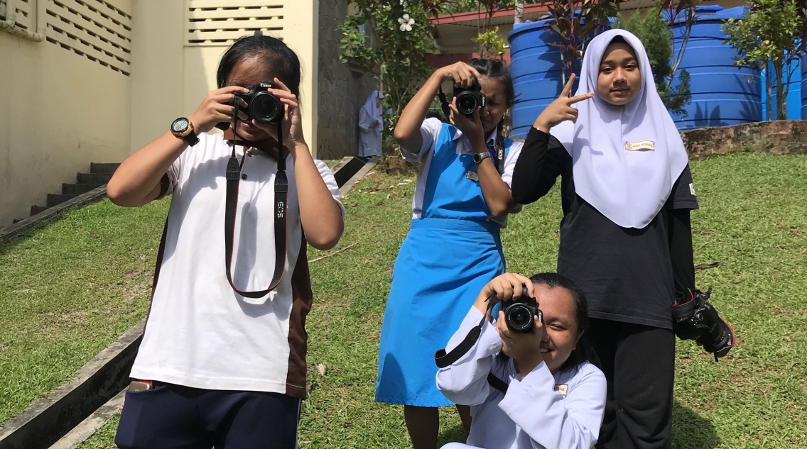 Four girls with light brown skin tone point cameras towards us