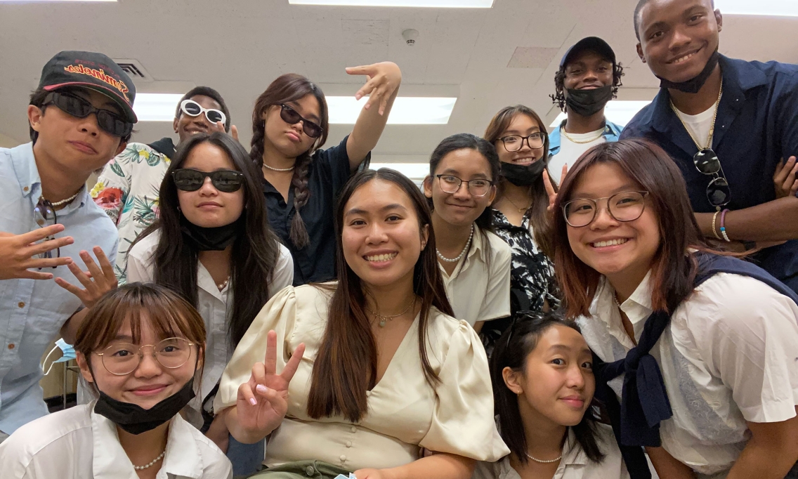 A group of teenagers huddle together and smile for the camera.