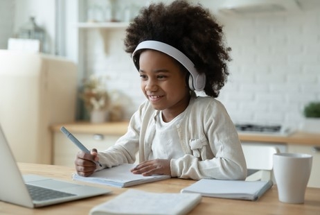 Photo of a girl wearing headphones and viewing something on a laptop while taking notes