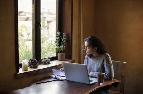 Picture of a woman sitting at a table, with a laptop and notebook on the table.