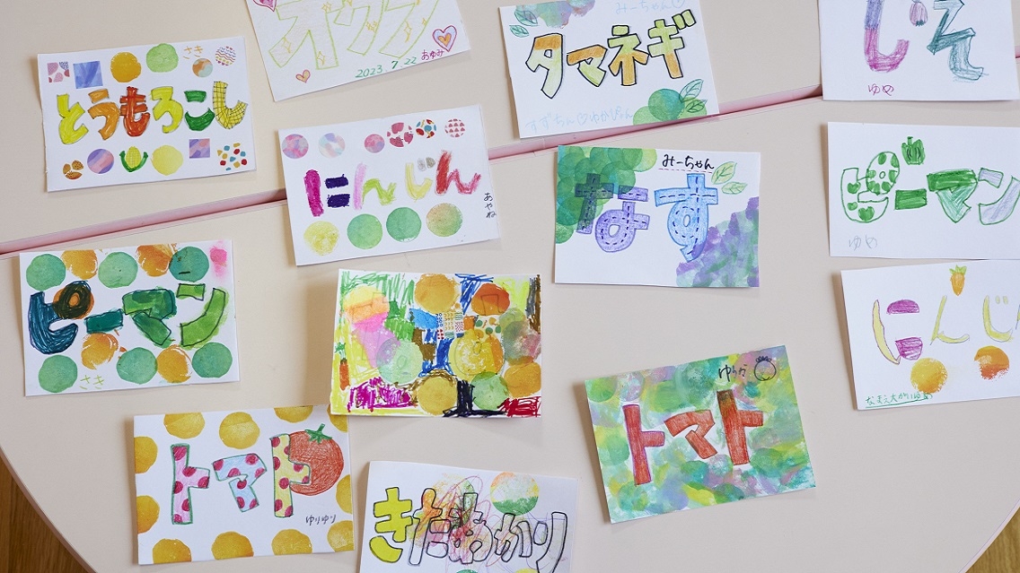 12 colorful paintings with Japanese writing sit on a white table.
