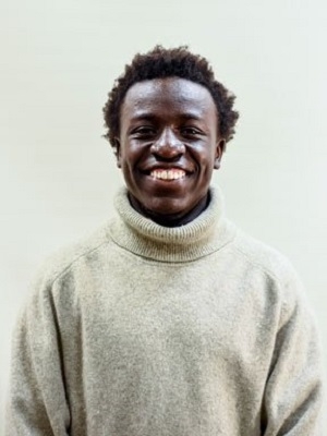 Patrick Kuruga wearing a white sweater, smiling at the camera.